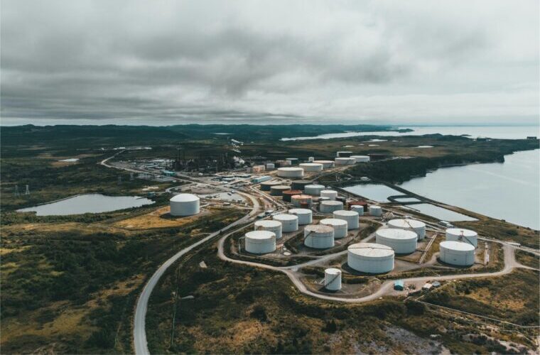 Aerial landscape shot of a coastal oil refinery with storage silos under cloudy skies.